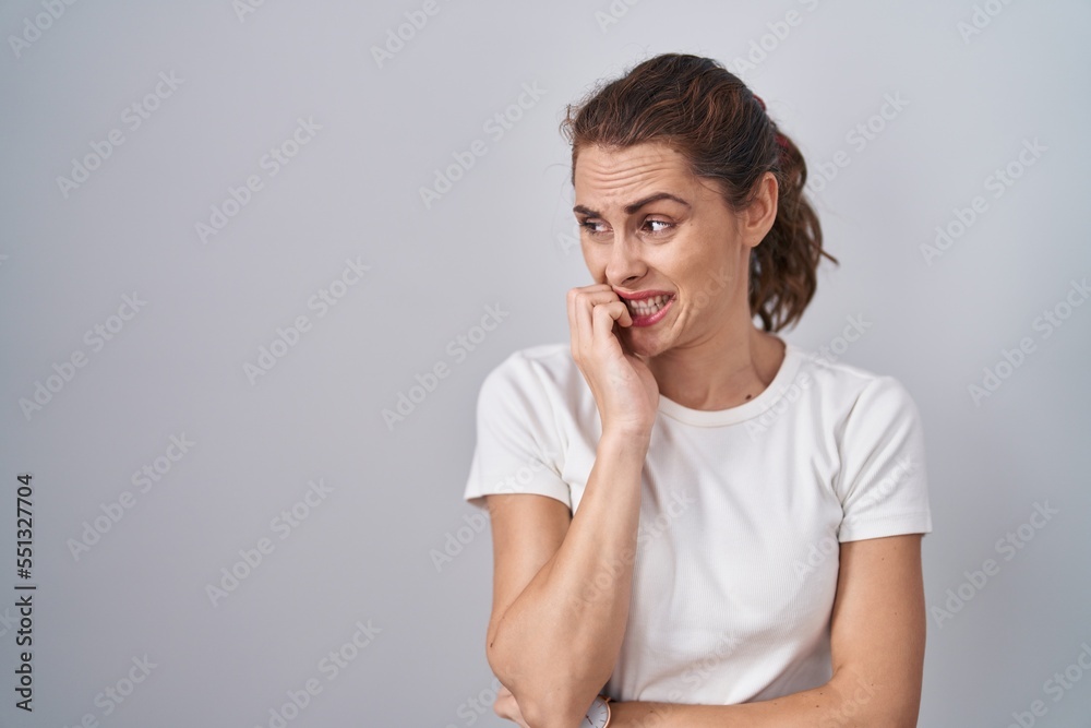 Beautiful brunette woman standing over isolated background looking stressed and nervous with hands on mouth biting nails. anxiety problem. Beautiful brunette woman standing over isolated background looking stressed and nervous with hands on mouth biting nails. anxiety problem.