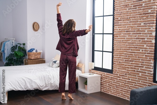 Young woman stretching arms standing on back view at bedroom