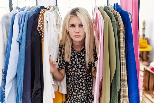 Young blonde woman searching clothes on clothing rack depressed and worry for distress, crying angry and afraid. sad expression.