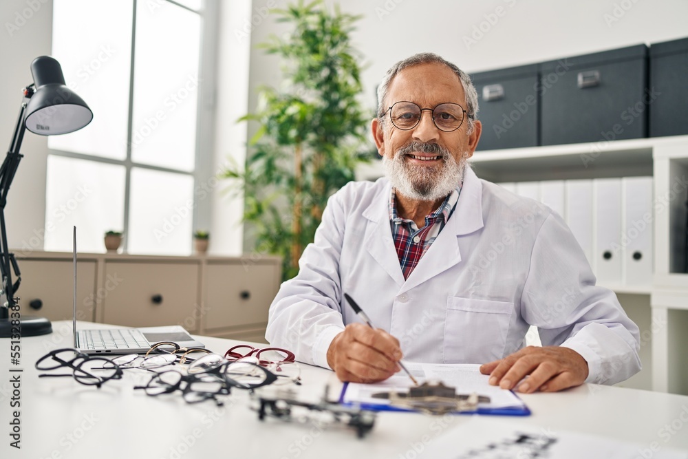 Senior grey-haired man optician writing on document at clinic Senior grey-haired man optician writing on document at clinic