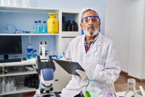 Senior grey-haired man scientist writing report working at laboratory
