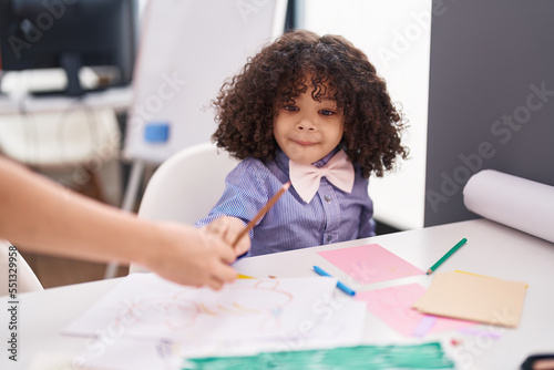 African american toddler preschool student sitting on table holding color pencil at kindergarten