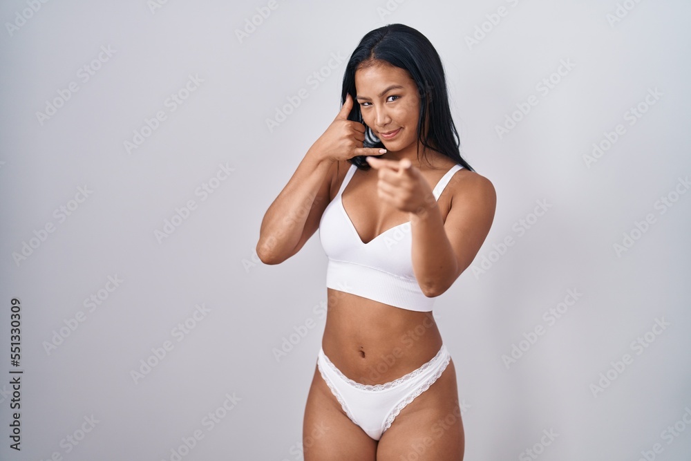 Hispanic woman wearing lingerie smiling doing talking on the telephone gesture and pointing to you. call me. Hispanic woman wearing lingerie smiling doing talking on the telephone gesture and pointing to you. call me.