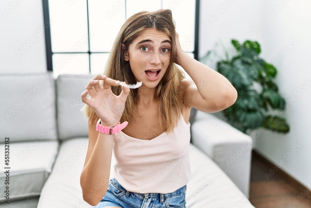 Young blonde woman holding invisible aligner orthodontic crazy and scared with hands on head, afraid and surprised of shock with open mouth Young blonde woman holding invisible aligner orthodontic crazy and scared with hands on head, afraid and surprised of shock with open mouth