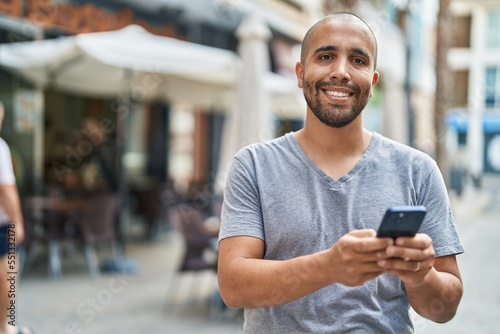Young latin man smiling confident using smartphone at coffee shop terrace