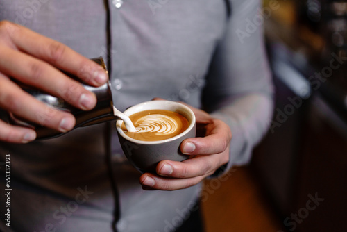 Barman making coffee  latte art in coffee shop. Close up of the man holding coffee cup and making art