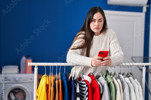 Young brunette woman waiting for laundry using smartphone skeptic and nervous, frowning upset because of problem. negative person.