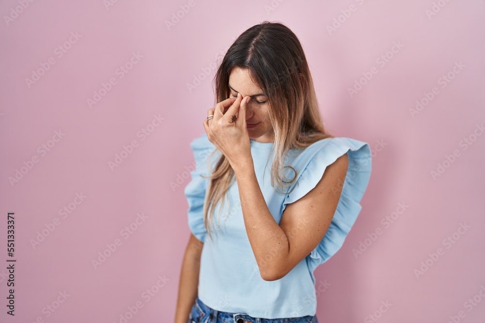 Young hispanic woman standing over pink background tired rubbing nose and eyes feeling fatigue and headache. stress and frustration concept. Young hispanic woman standing over pink background tired rubbing nose and eyes feeling fatigue and headache. stress and frustration concept.