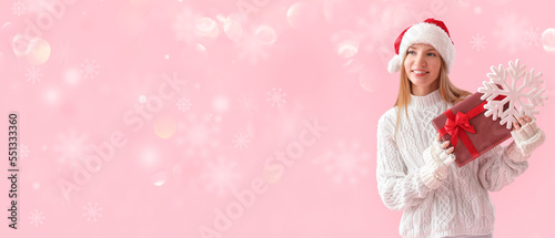 Pretty young woman in Santa hat holding Christmas present and snowflake on pink background with space for text