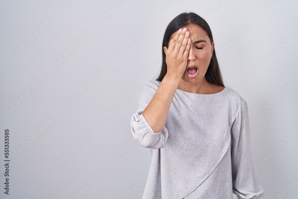 Young hispanic woman standing over white background yawning tired covering half face, eye and mouth with hand. face hurts in pain.