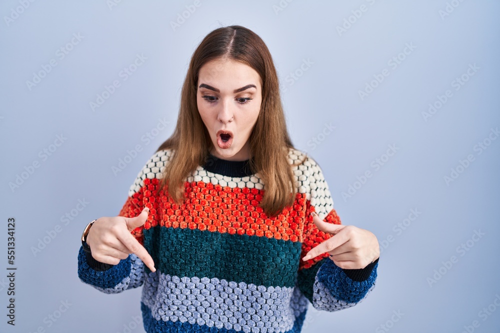 Young hispanic girl standing over blue background pointing down with fingers showing advertisement, surprised face and open mouth Young hispanic girl standing over blue background pointing down with fingers showing advertisement, surprised face and open mouth