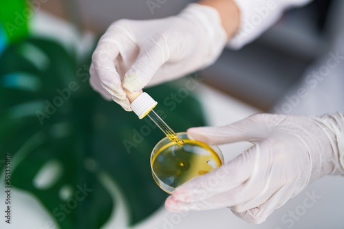 Young beautiful hispanic woman scientist pouring liquid on sample at laboratory