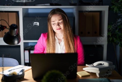 Young caucasian woman working at the office at night with hand on stomach because nausea, painful disease feeling unwell. ache concept.