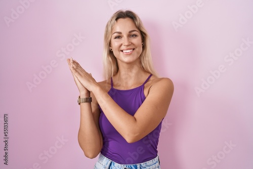 Young blonde woman standing over pink background clapping and applauding happy and joyful, smiling proud hands together