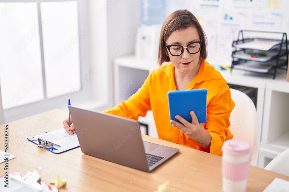 Middle age woman business worker using touchpad writing on document at office Middle age woman business worker using touchpad writing on document at office