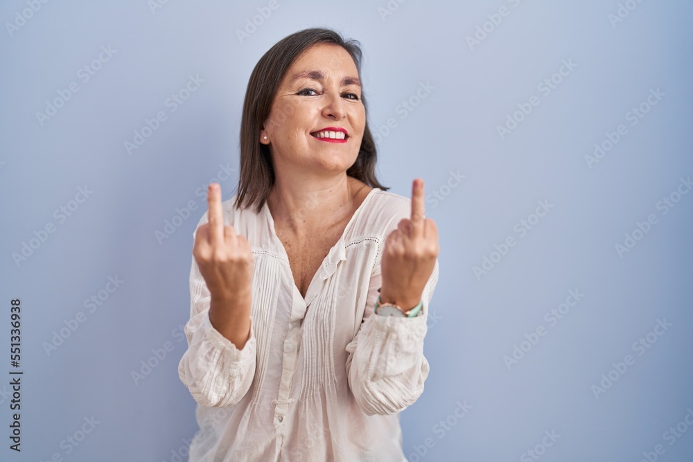 Middle age hispanic woman standing over blue background showing middle finger doing fuck you bad expression, provocation and rude attitude. screaming excited Middle age hispanic woman standing over blue background showing middle finger doing fuck you bad expression, provocation and rude attitude. screaming excited