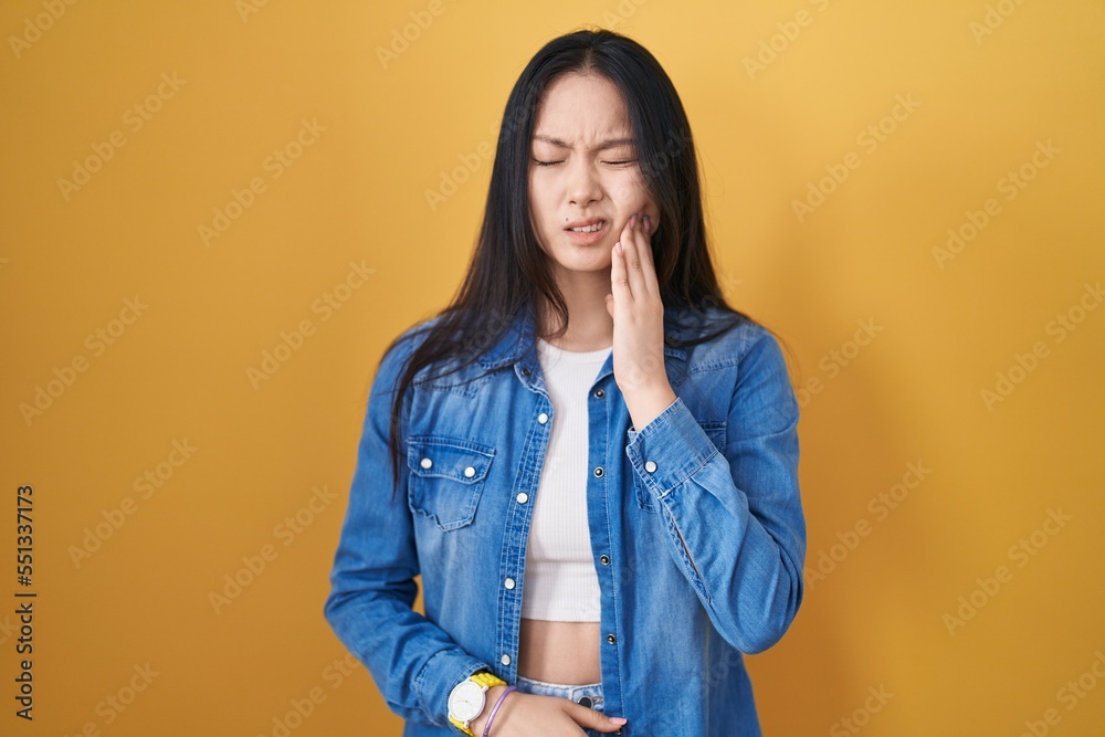 Young asian woman standing over yellow background touching mouth with hand with painful expression because of toothache or dental illness on teeth. dentist Young asian woman standing over yellow background touching mouth with hand with painful expression because of toothache or dental illness on teeth. dentist