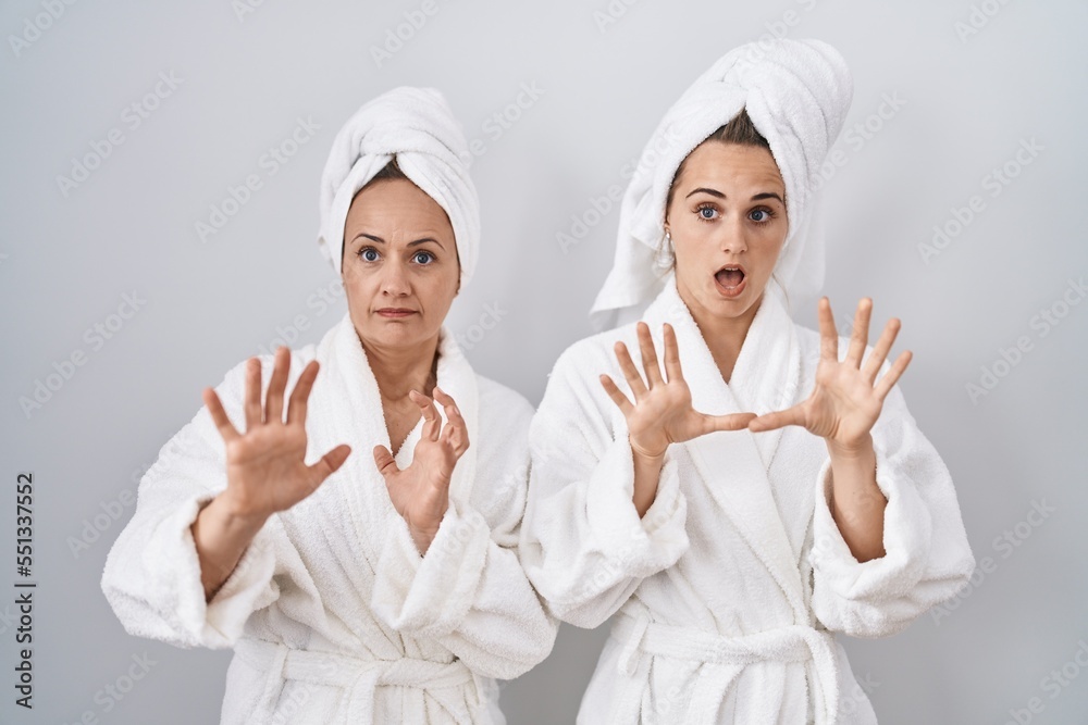Middle age woman and daughter wearing white bathrobe and towel afraid and terrified with fear expression stop gesture with hands, shouting in shock. panic concept. Middle age woman and daughter wearing white bathrobe and towel afraid and terrified with fear expression stop gesture with hands, shouting in shock. panic concept.