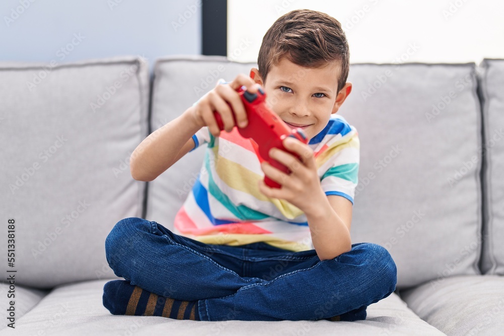 Blond child playing video game sitting on sofa at home Blond child playing video game sitting on sofa at home