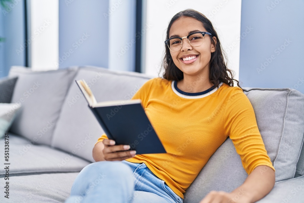 Young african american woman reading book sitting on sofa at home Young african american woman reading book sitting on sofa at home