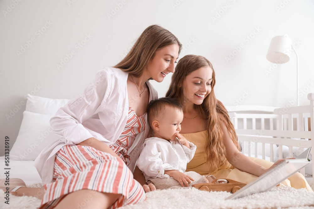 Happy lesbian couple reading story to their little baby in bedroom Happy lesbian couple reading story to their little baby in bedroom