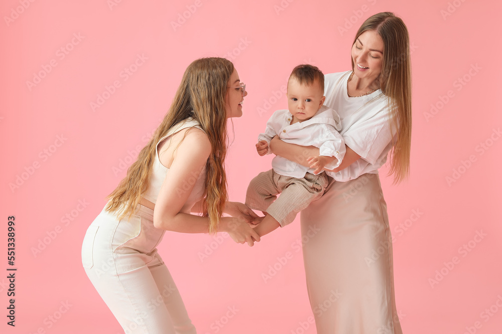 Happy lesbian couple with their little baby on pink background Happy lesbian couple with their little baby on pink background