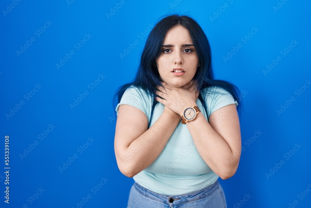 Young modern girl with blue hair standing over blue background shouting suffocate because painful strangle. health problem. asphyxiate and suicide concept.