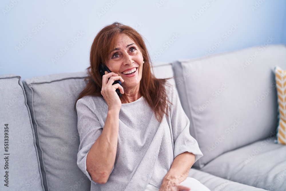 Middle age woman talking on the smartphone sitting on sofa at home