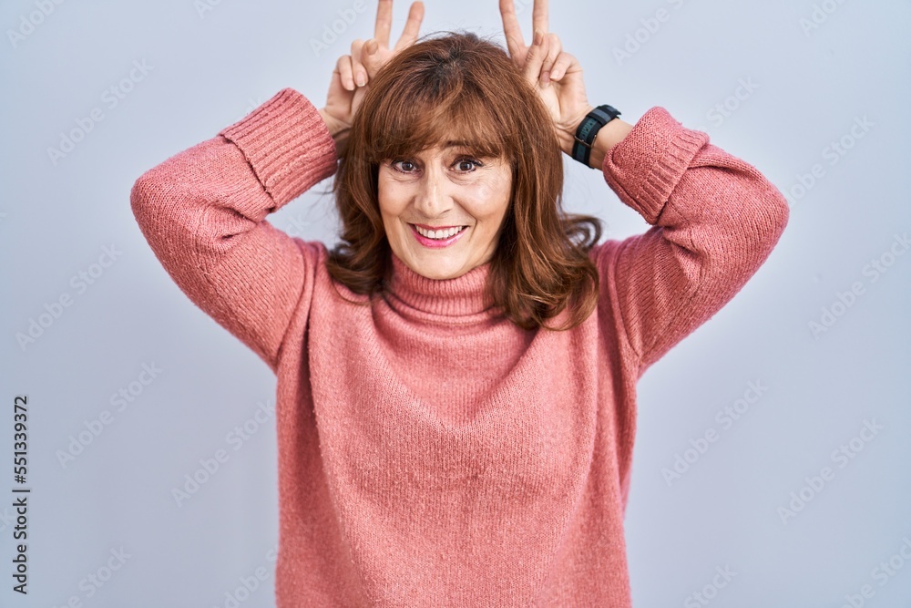 Middle age hispanic woman standing over isolated background posing funny and crazy with fingers on head as bunny ears, smiling cheerful Middle age hispanic woman standing over isolated background posing funny and crazy with fingers on head as bunny ears, smiling cheerful