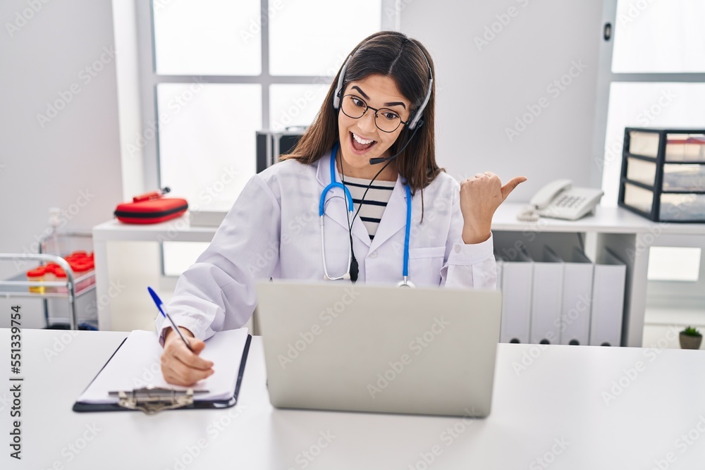 Young brunette woman working on online appointment pointing thumb up to the side smiling happy with open mouth Young brunette woman working on online appointment pointing thumb up to the side smiling happy with open mouth