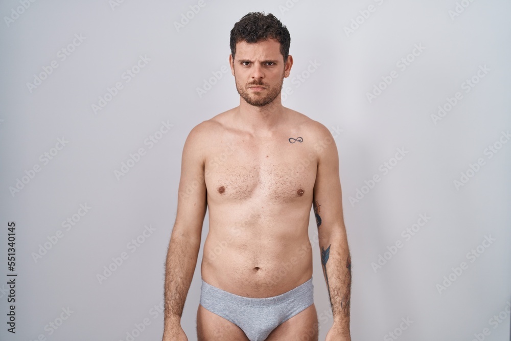 Young hispanic man standing shirtless wearing underware skeptic and nervous, frowning upset because of problem. negative person.