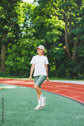 A young woman in a white t-shirt and sneakers, a cap on her head. She is warming up before training outdoors at the stadium. Healthy lifestyle © Дмитрий Ткачук