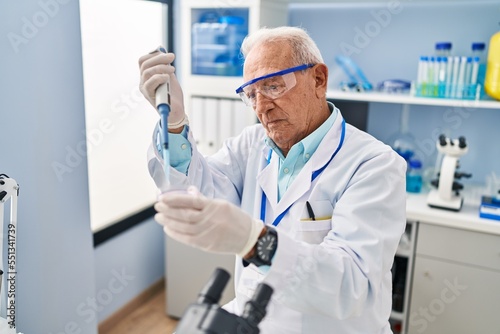 Senior man wearing scientist uniform using pipette working at laboratory
