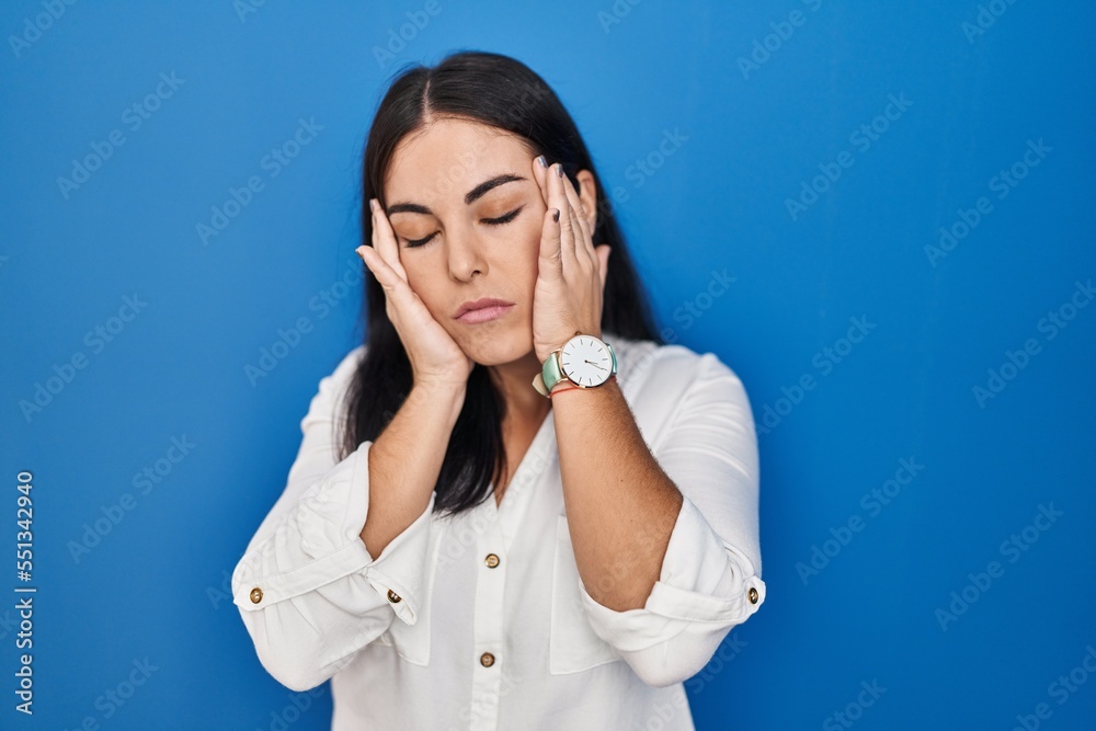 Young hispanic woman standing over blue background tired hands covering face, depression and sadness, upset and irritated for problem