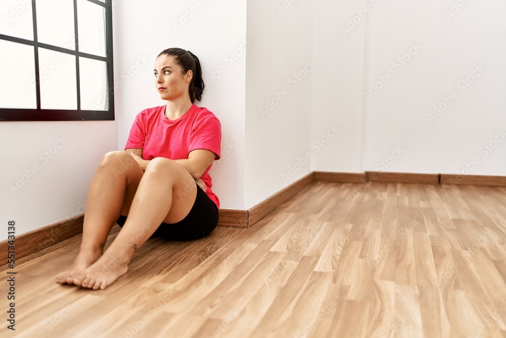 Young beautiful hispanic woman sitting on floor with serious expression at empty room Young beautiful hispanic woman sitting on floor with serious expression at empty room