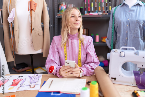 Young blonde woman tailor smiling confident using smartphone at tailor shop