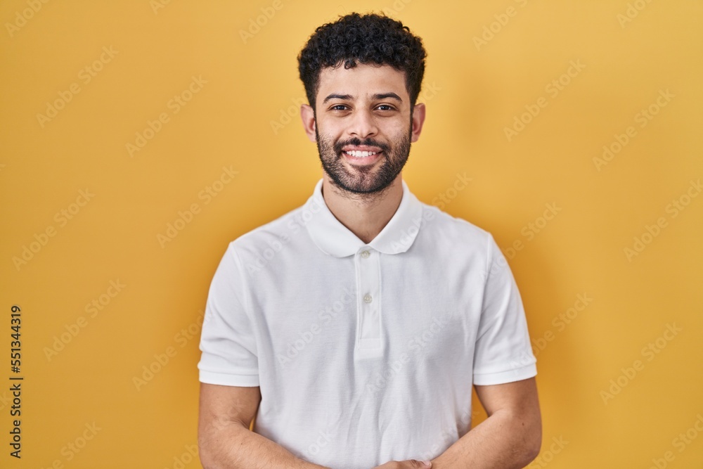 Arab man standing over yellow background with hands together and crossed fingers smiling relaxed and cheerful. success and optimistic Arab man standing over yellow background with hands together and crossed fingers smiling relaxed and cheerful. success and optimistic