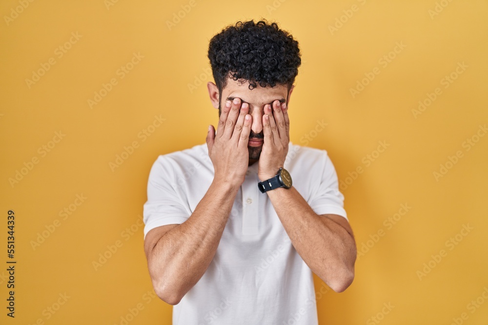 Arab man standing over yellow background rubbing eyes for fatigue and headache, sleepy and tired expression. vision problem