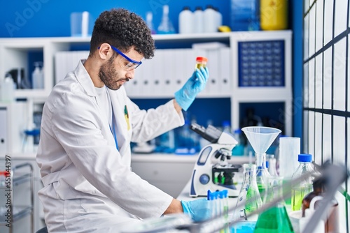 Young arab man wearing scientist uniform holding urine test tube at laboratory