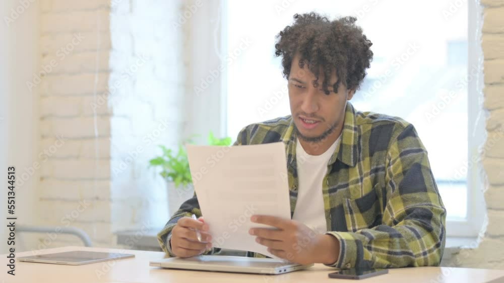 Young African Man Reading Documents in Office, Doing Paperwork Young African Man Reading Documents in Office, Doing Paperwork
