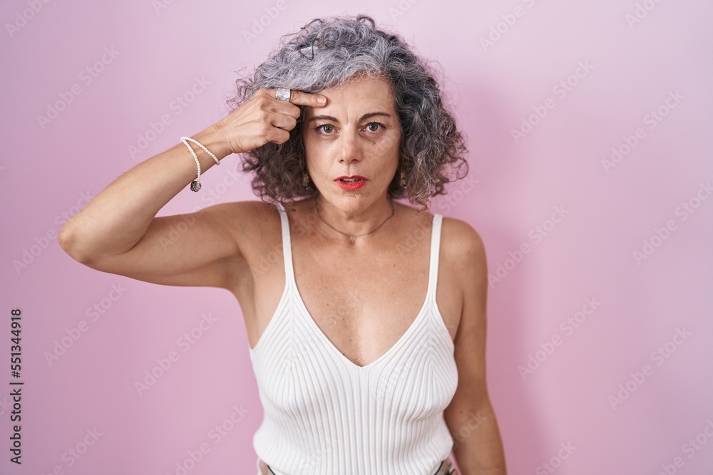 Middle age woman with grey hair standing over pink background pointing unhappy to pimple on forehead, ugly infection of blackhead. acne and skin problem Middle age woman with grey hair standing over pink background pointing unhappy to pimple on forehead, ugly infection of blackhead. acne and skin problem