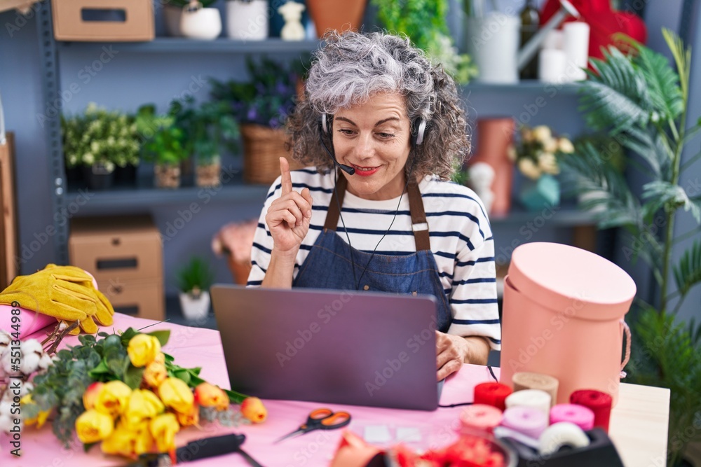 Fototapeta premium Middle age woman with grey hair working at florist with laptop smiling with an idea or question pointing finger with happy face, number one