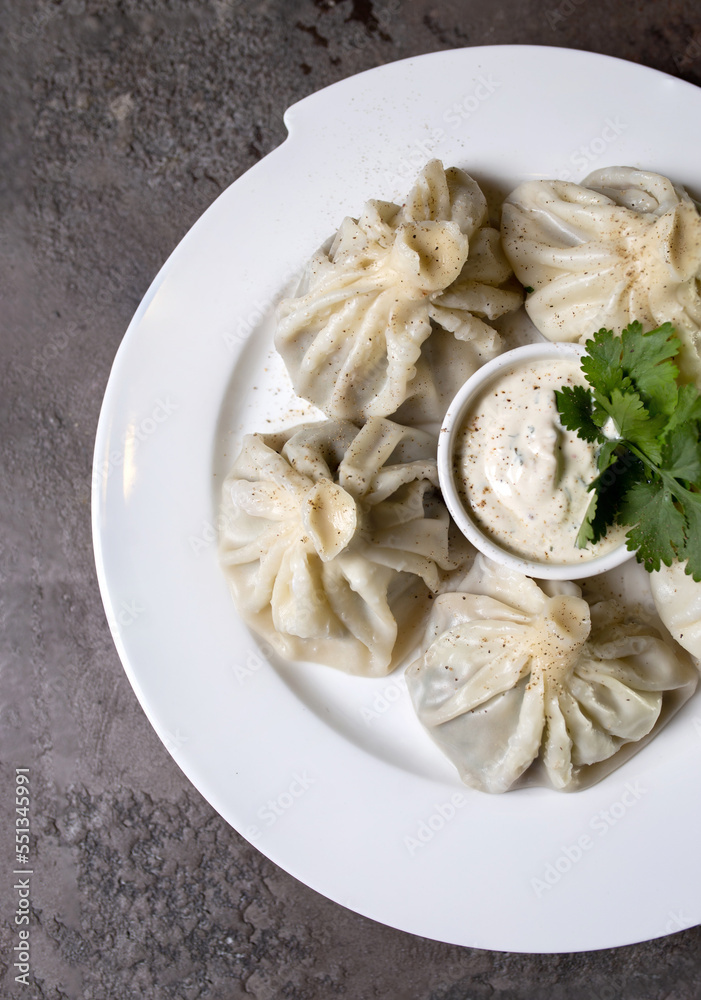 khinkali on a white plate with sauce and herbs on a gray background khinkali on a white plate with sauce and herbs on a gray background