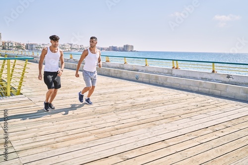 Fototapeta Naklejka Na Ścianę i Meble -  Two hispanic men sporty couple smiling confident running at seaside