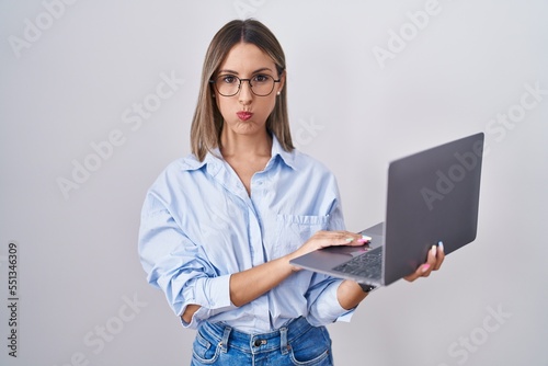 Young woman working using computer laptop puffing cheeks with funny face. mouth inflated with air, crazy expression.