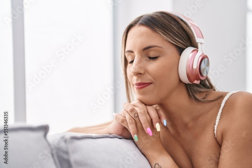 Young beautiful hispanic woman listening to music sitting on sofa at home