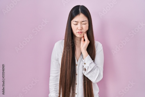 Chinese young woman standing over pink background touching mouth with hand with painful expression because of toothache or dental illness on teeth. dentist