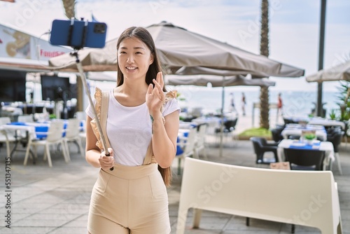 Young chinese girl smiling happy having video call using smartphone at the promenade. © Krakenimages.com