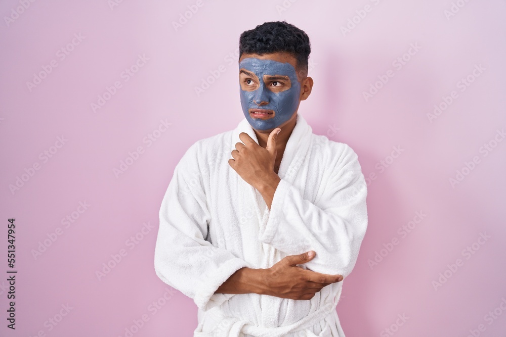Young hispanic man wearing beauty face mask and bath robe thinking worried about a question, concerned and nervous with hand on chin Young hispanic man wearing beauty face mask and bath robe thinking worried about a question, concerned and nervous with hand on chin