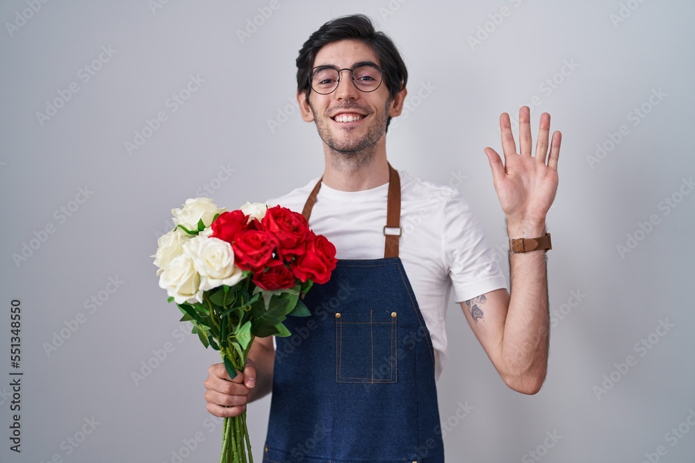 Young hispanic man holding bouquet of white and red roses waiving saying hello happy and smiling, friendly welcome gesture Young hispanic man holding bouquet of white and red roses waiving saying hello happy and smiling, friendly welcome gesture